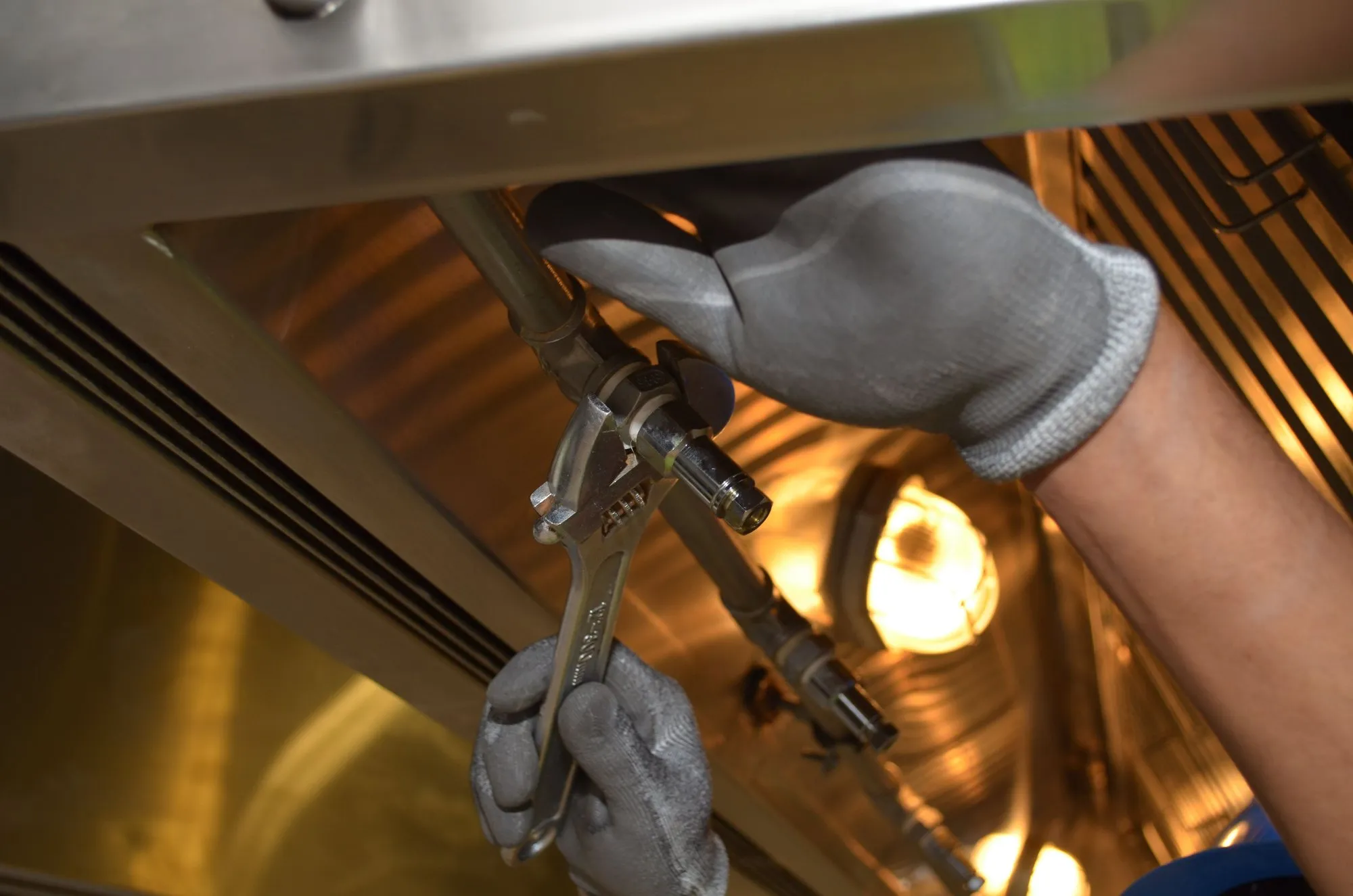 Gloved hands tightening a pipe fitting with a wrench